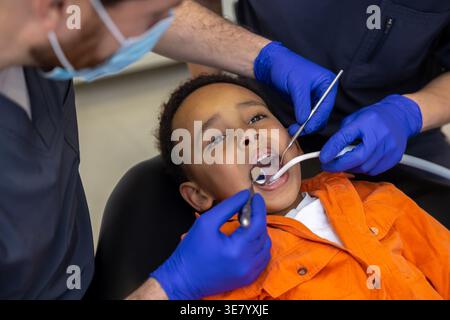 Schwarzer Junge bei zahnärztlicher Behandlung mit kaukasischen männlichen Zahnärzten in der Klinik Stockfoto