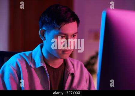 Asiatischer Mann, der auf den Computer auf dem Tisch schaut und zu Hause im Stuhl sitzt Stockfoto