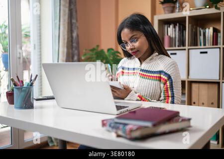 Afroamerikanische Studentin sitzt am Tisch und besucht zu Hause den Online-Kurs Stockfoto