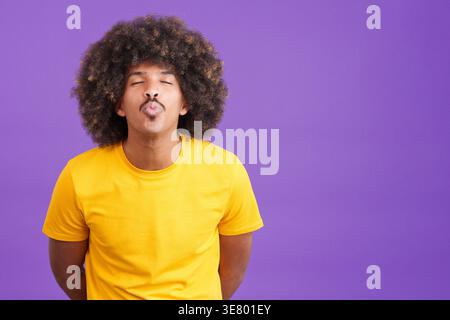 Gemischter Rassenmann mit geschlossenen Augen, der Küsse bläst, während er vor violettem Hintergrund steht Stockfoto