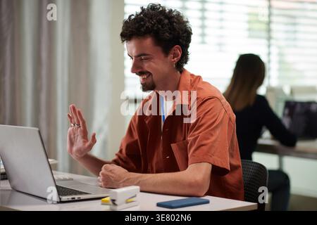 Lächelnder Geschäftsmann mit gemischter Rasse, der Videoanrufe hat, während er am Tisch im Büro sitzt Stockfoto