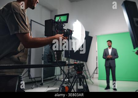Ein Kameramann mit gemischter Rasse, der einen Black man-Journalisten aufnimmt, der Nachrichten für das Fernsehprogramm im Studio berichtet Stockfoto