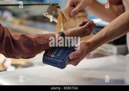 Hände einer Frau aus gemischter Rasse, die mit Smartwatch zum Mitnehmen bestellt, während sie an der Theke in der Bäckerei steht Stockfoto