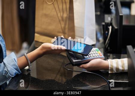 Nahaufnahme von Black Woman, die das Smartphone benutzt, um im Geschäft zu bezahlen Stockfoto