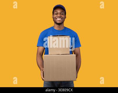 Schwarzer Liefermann, der Boxen hält, die vor gelbem Hintergrund im Studio stehen Stockfoto