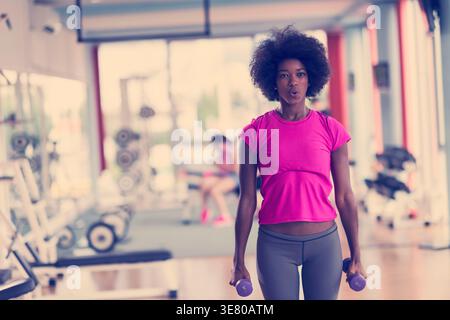 Schwarze Frau mit Afro, die mit Hanteln im Fitnessstudio Sport macht Stockfoto