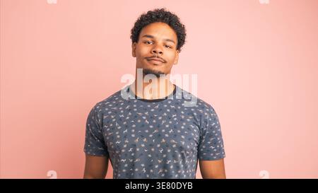 Gemischter Mann mit lockigem Haar, der im Studio vor rosa Hintergrund steht Stockfoto