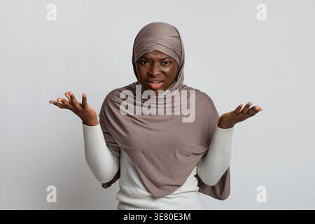 Enttäuschte schwarze muslimische Frau im Hijab, die Hände vor grauem Hintergrund im Atelier spreizt Stockfoto