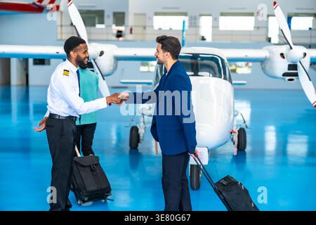 Afroamerikanischer Pilot schüttelt Hand mit Geschäftsmann, der in der Nähe des Privatjets im Hangar steht Stockfoto