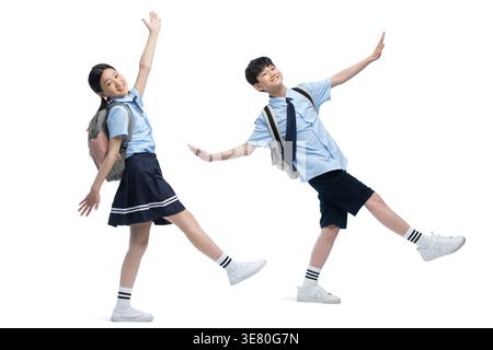 Chinesische Schüler und Mädchen spreizen Arme, während sie mit einem Bein vor weißem Hintergrund im Studio stehen Stockfoto