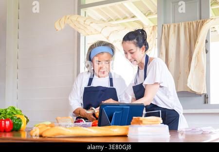 Asiatische Frau mittleren Alters, die Essen zubereitete, mit einer älteren Mutter, die in der Küche am Tisch stand Stockfoto