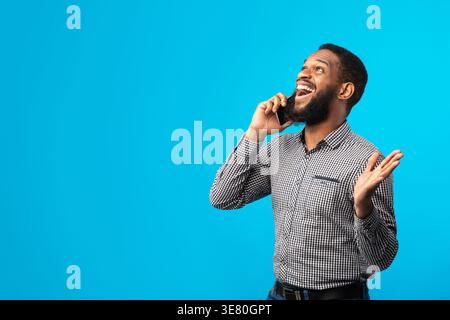 Überraschter Schwarzer, der einen Anruf hatte, während er im Studio vor blauem Hintergrund stand Stockfoto