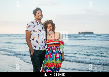 Hispanische Frau mittleren Alters mit lockigen Haaren, die bunt mit ihrem Sohn am Strand steht Stockfoto