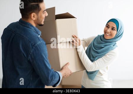 Mann aus dem Nahen Osten und muslimische Frau im Hijab stehen und tragen Papierkästen zusammen, während sie in ihr neues Haus ziehen Stockfoto