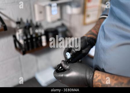 Hispanischer männlicher Tätowierer, der schwarze Nitrilhandschuhe trägt und seine Tätowiermaschine reinigt, während er im Studio steht Stockfoto
