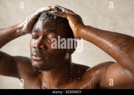 Schwarzer Mann, der Shampoo auf die Haare aufträgt, während er im Badezimmer zu Hause duscht Stockfoto