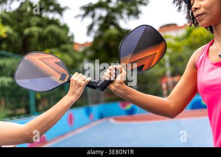 Verschiedene Freundinnen schlagen gegen Schläger, bevor sie tagsüber auf dem Hof pickleball spielen Stockfoto