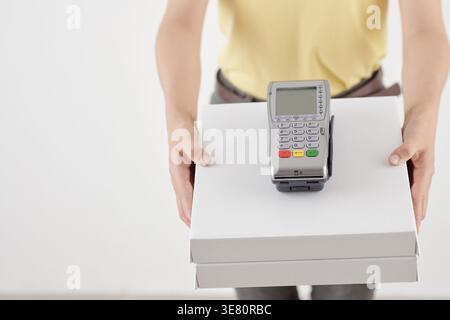 Lieferfrau übergibt Kästen mit Zahlungsterminal vor weißem Hintergrund Stockfoto