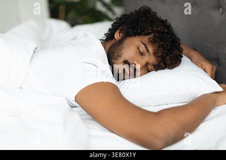 Bärtiger indischer Mann mit lockigen Haaren, der im Schlafzimmer zu Hause auf dem Bett schläft Stockfoto