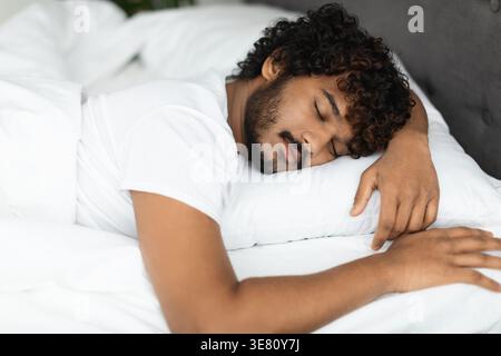 Bärtiger indischer Mann mit lockigen Haaren, der im Schlafzimmer zu Hause auf dem Bett schläft Stockfoto