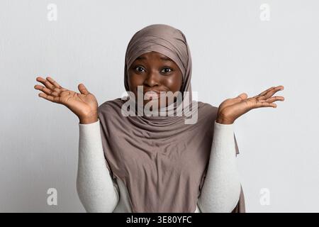 Enttäuschte schwarze muslimische Frau im Hijab, die Hände vor grauem Hintergrund im Atelier spreizt Stockfoto