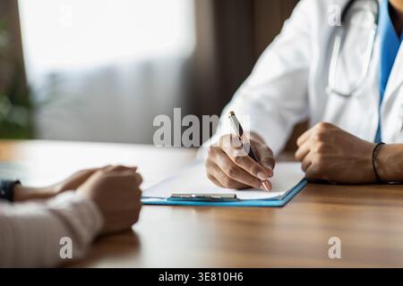 Zugeschnittenes Bild eines schwarzen männlichen Arztes, der in der Klinik Rezepte auf der Akte schreibt Stockfoto