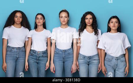 Verschiedene Frauen in weißen Hemden und Jeans stehen im Studio vor blauem Hintergrund Stockfoto