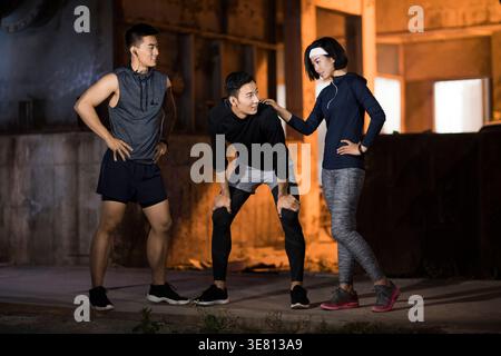 Lächelnde chinesische Freunde ruhen sich nach dem Laufen aus, während sie nachts zusammen auf der Straße stehen Stockfoto