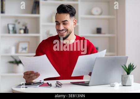 Arabischer Mann, der an Dokumenten arbeitet, sitzt am Schreibtisch mit Laptop zu Hause Stockfoto