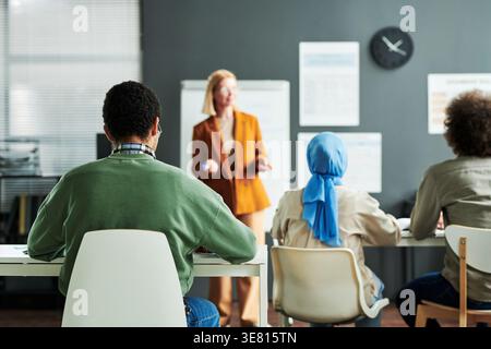 Rückansicht eines gemischten männlichen Schülers, der sich Notizen über die Diskussion macht, während er im Klassenzimmer am Tisch sitzt Stockfoto