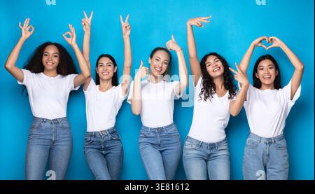 Verschiedene Frauengruppen in weißen Hemden und Jeans, die verschiedene Handgesten zeigen, während sie im Studio vor blauem Hintergrund stehen Stockfoto