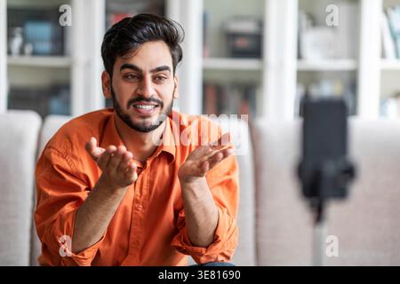 Männlicher Vlogger aus dem Mittleren Osten, der Hände mit Gesten aufnimmt, um Videos zu Hause auf dem Sofa zu machen Stockfoto