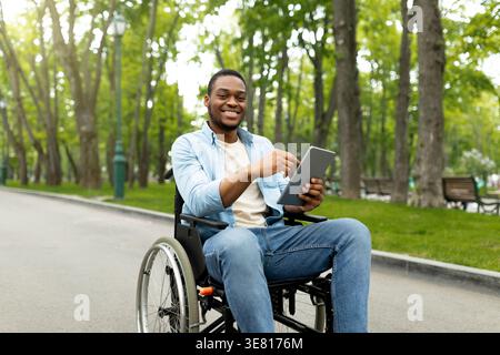Schwarzer Mann im Rollstuhl mit Tablet im Park Stockfoto