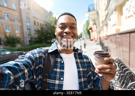 Schwarzer Mann, der eine Kaffeetasse hält und Selfie macht, der am sonnigen Tag auf der Straße steht Stockfoto