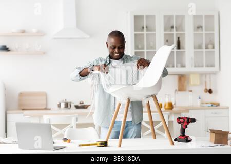 Schwarzer Mann, der Plastik auf Stuhl entfernt und Möbel auspackt, die zu Hause in der Küche stehen Stockfoto