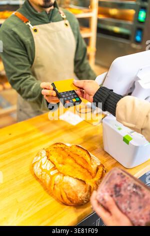 Zugeschnittenes Bild einer hispanischen Kundin, die Brot kauft und mit Kreditkarte bezahlt, während sie an der Theke in der Bäckerei steht Stockfoto