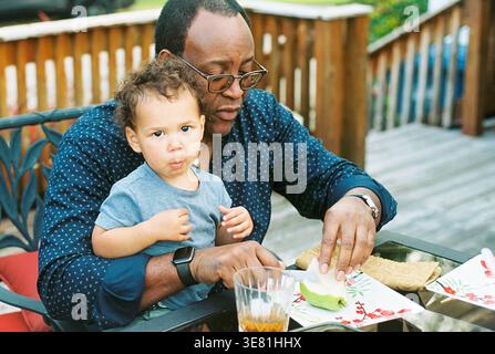 Afroamerikanischer Großvater mit Enkel, der draußen auf dem Tisch isst Stockfoto