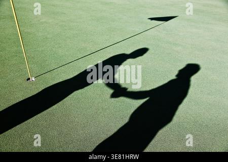 Schatten von älteren Golfern, die in der Nähe der Fahnenstange auf dem Golfplatz stehen Stockfoto
