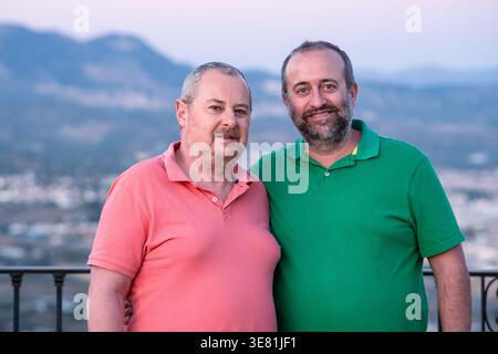 Lächelndes hispanisches und älteres kaukasisches männliches Paar mittleren Alters, das bei Sonnenuntergang zusammen im Freien steht Stockfoto