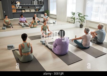 Gruppe von Personen, die auf Trainingsmatten sitzen und mit einem Lehrer im Yoga-Kurs trainieren Stockfoto
