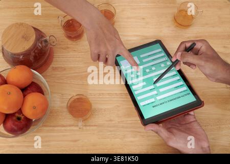 Indischer männlicher Versicherungsagent hilft Kunden, Informationen mit einem Tablet zu füllen, das auf dem Sofa zu Hause sitzt Stockfoto