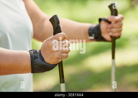 Nahaufnahme der Hände einer Schwarzen Frau, die beim Spaziergang im Park nordische Stöcke hält Stockfoto