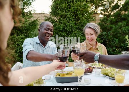 Verschiedene Familien toasten Weingläser, während sie während des Mittagessens im Hinterhof zu Hause am Tisch sitzen Stockfoto