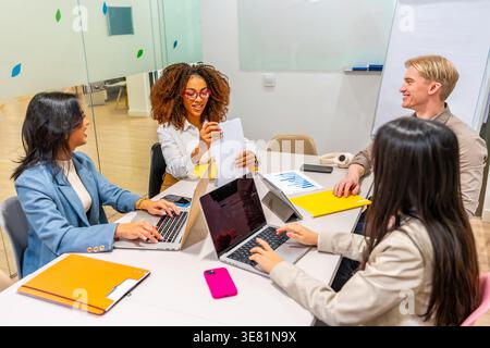 Verschiedene Kollegen diskutieren die Geschäftsstrategie mithilfe von Laptops, während sie während der Besprechung im Büro zusammen am Tisch sitzen Stockfoto