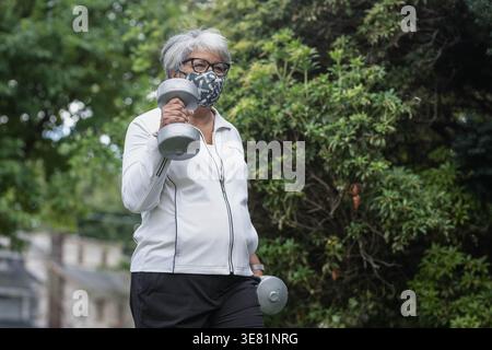 Ältere schwarze Frau mit Gesichtsmaske, die mit Kurzhanteln arbeitet Stockfoto