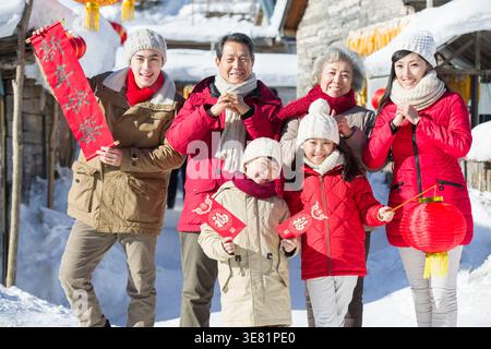 Lächelnde chinesische Familie in warmen Jacken feiert das chinesische Neujahr, während sie im Winter in der verschneiten Straße steht Stockfoto