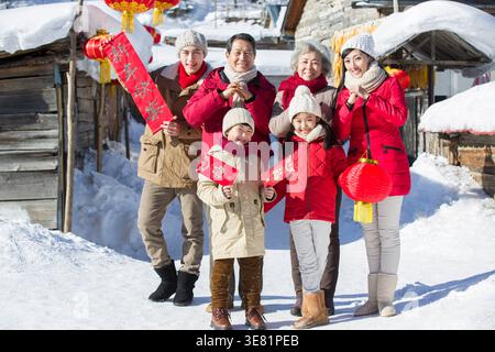 Lächelnde chinesische Familie in warmen Jacken feiert das chinesische Neujahr, während sie im Winter in der verschneiten Straße steht Stockfoto
