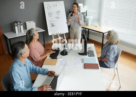 Asiatische Lehrerin, die erklärt, wie Internetverbindung für eine Gruppe von Senioren in der Schule funktioniert Stockfoto