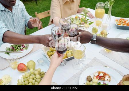 Zugeschnittenes Bild von verschiedenen Familien, die tagsüber Gläser beim Mittagessen im Garten trinken Stockfoto