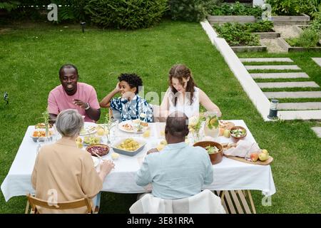 Vielfältige Familie, die tagsüber am Tisch im Hinterhof zu Mittag essen Stockfoto
